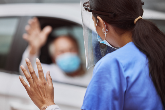 Nurse waving to a patient at a drive-through COVID-19 vaccine site