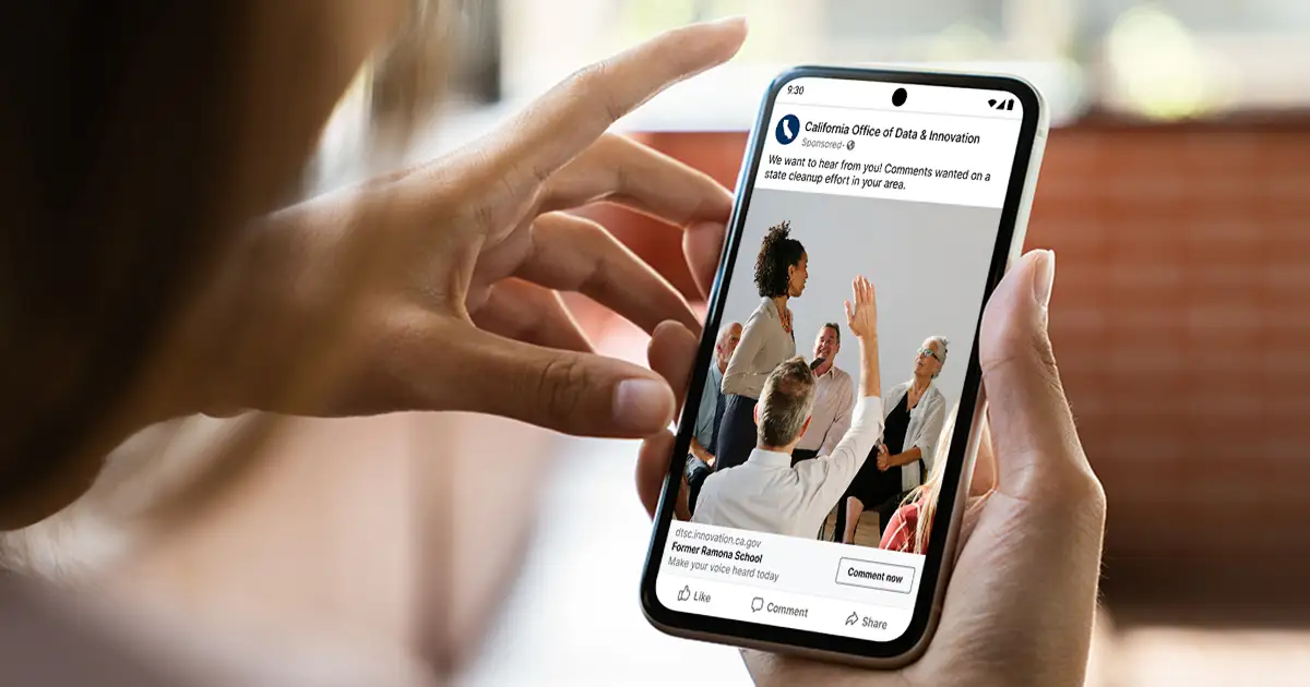 A mobile phone showing a Facebook add for the Former Ramona School cleanup project public comment period. The phone is being held in a hand as someone scrolls