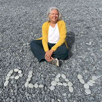 Virginia Hamilton sits on a pebble beach with rocks that spell out the word PLAY.