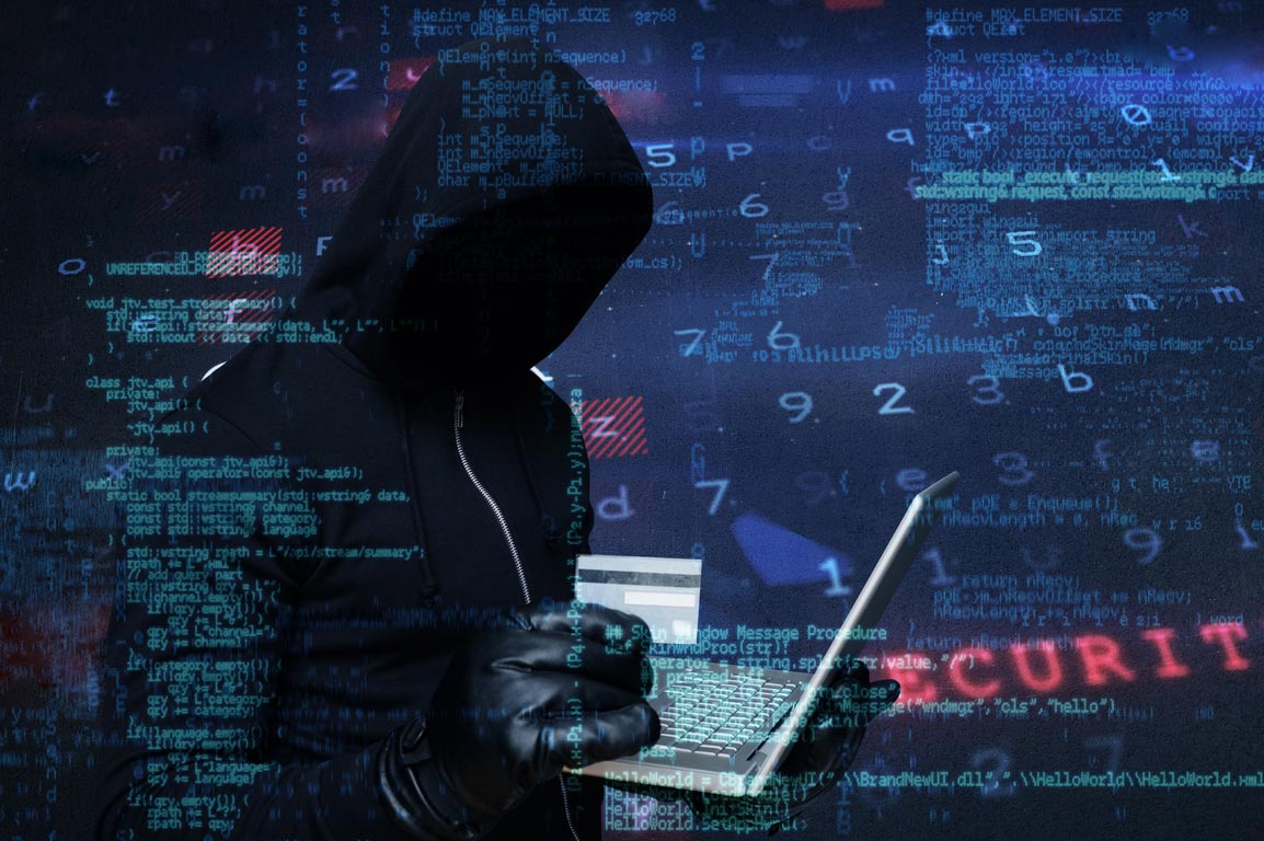 Hooded figure typing on laptop surrounded by computer code