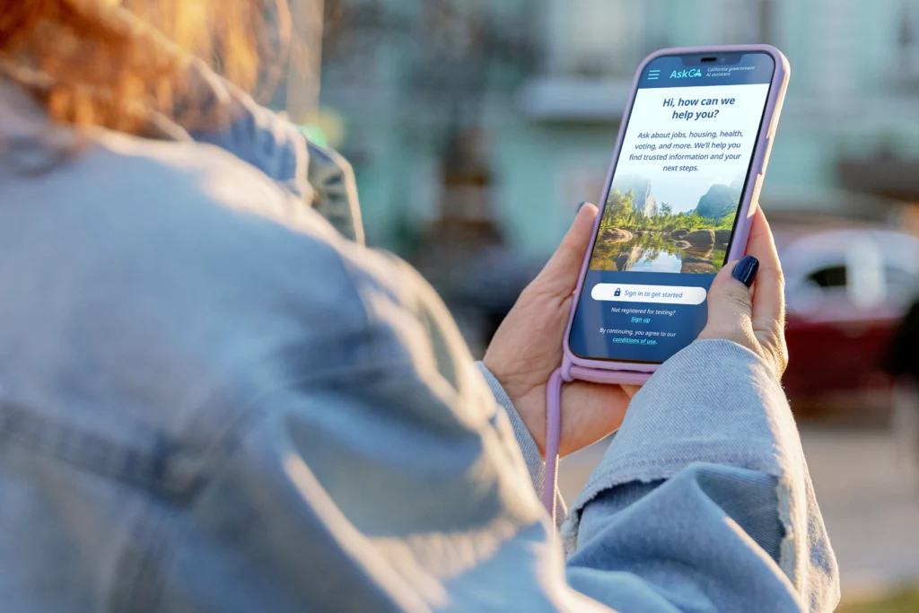 A woman holds a smartphone showing the AskCA sign in screen